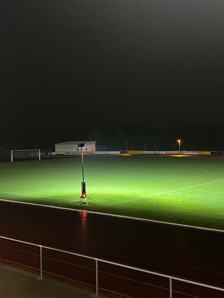 Ein BASELIGHT Lichtmast am Rand eines Sportplatzes leuchtet nachts den Rasen bis zum Tor aus