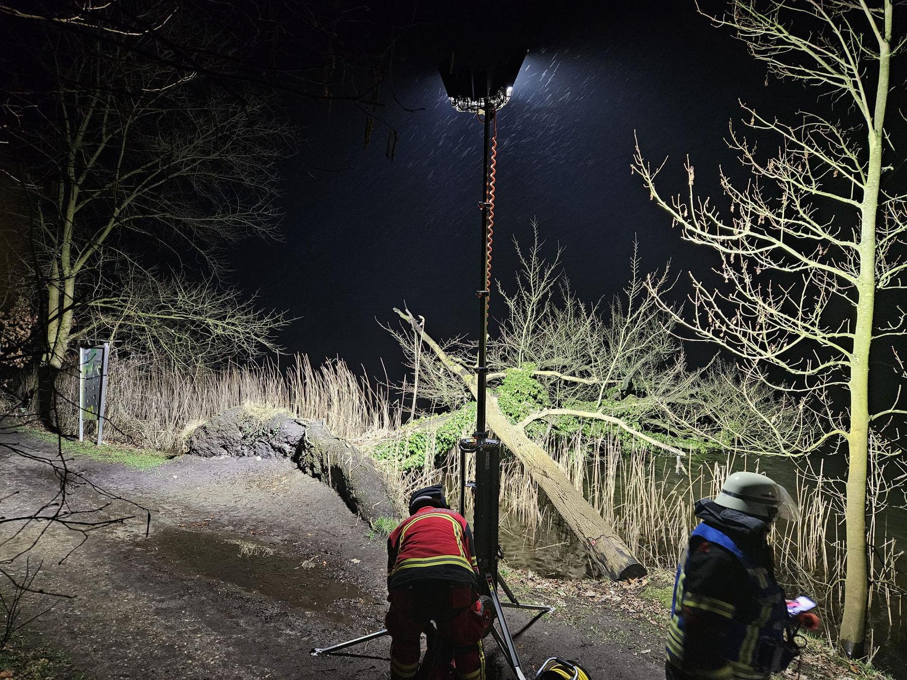 Feuerwehrleute bei Nacht an einem umgestürzten Baum am Ufer, ein BASELIGHT Lichtmast leuchtet die Stelle aus