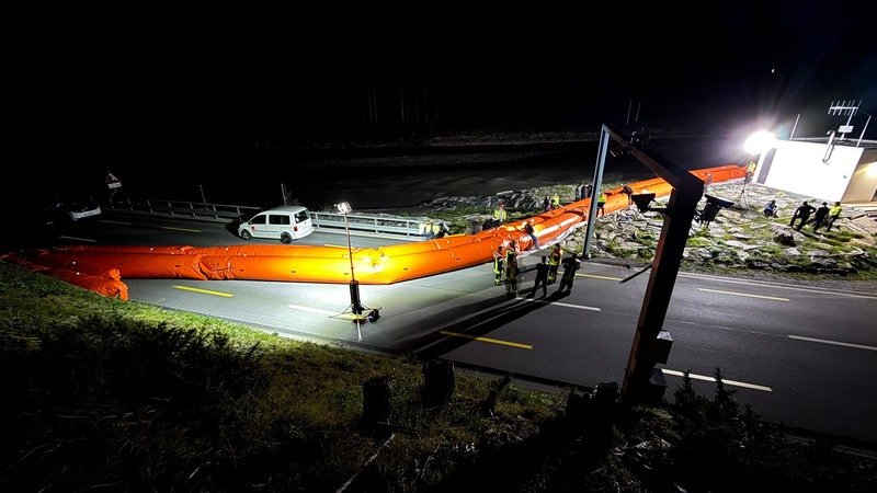 Hochwasserschutz bei Nacht, Einsatzkräfte an einer orangen Schlauchsperre auf der Straße, ein BASELIGHT Lichtmast leuchtet die Stelle aus